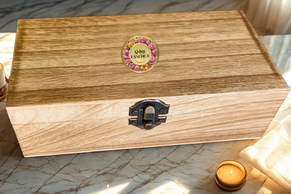 Closed Anne Essence wooden luxury gift box with branded floral logo, displayed on a marble surface with a lit candle beside it.